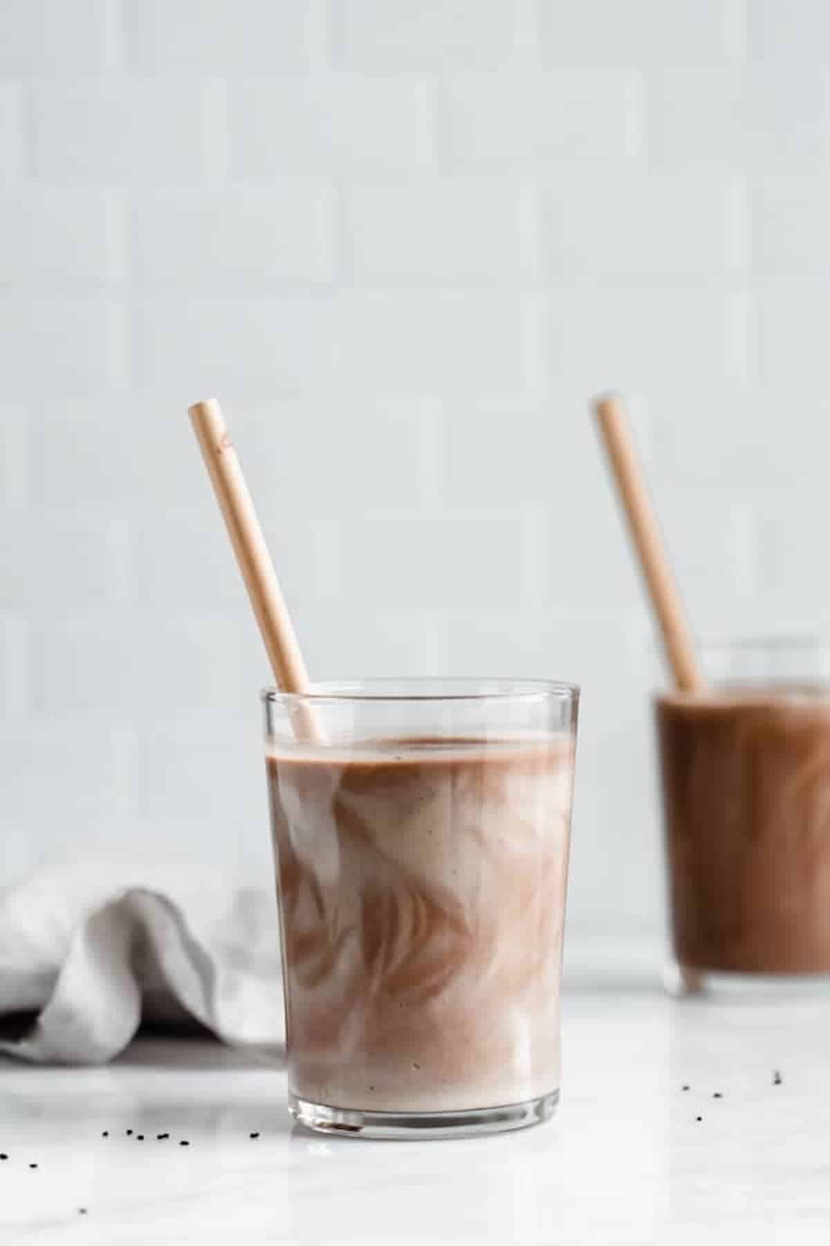 swirled chocolate shake in a clear glass with a brown paper straw against a white tile backdrop