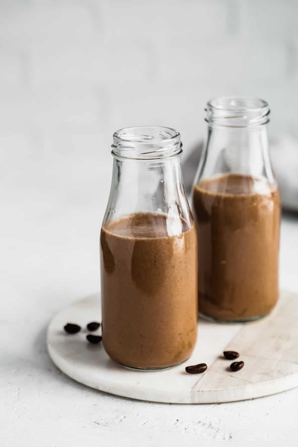 two milk jars filled with coffee smoothie on a serving board with fresh whole coffee beans