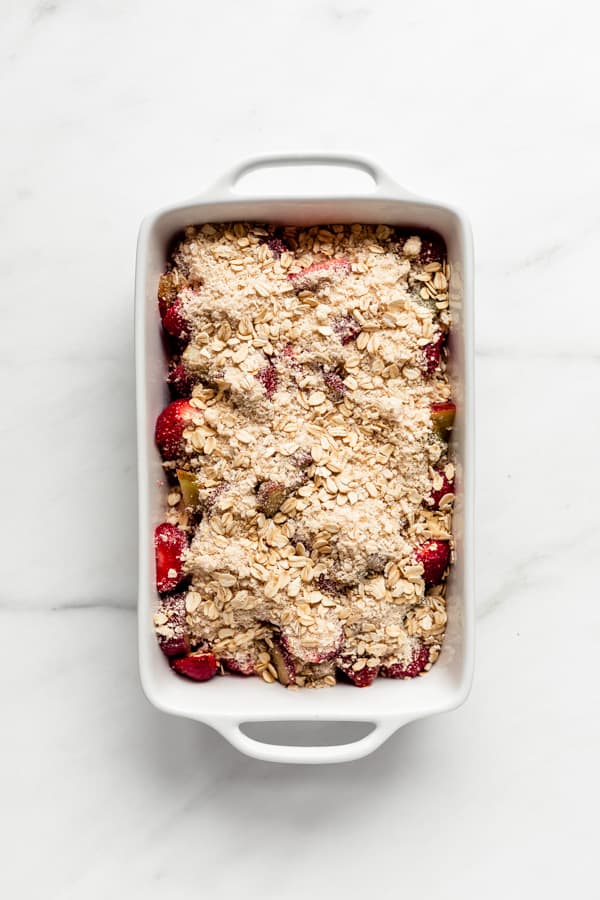 a white baking dish with strawberries and rhubarb in it topped with an oat crumble topping