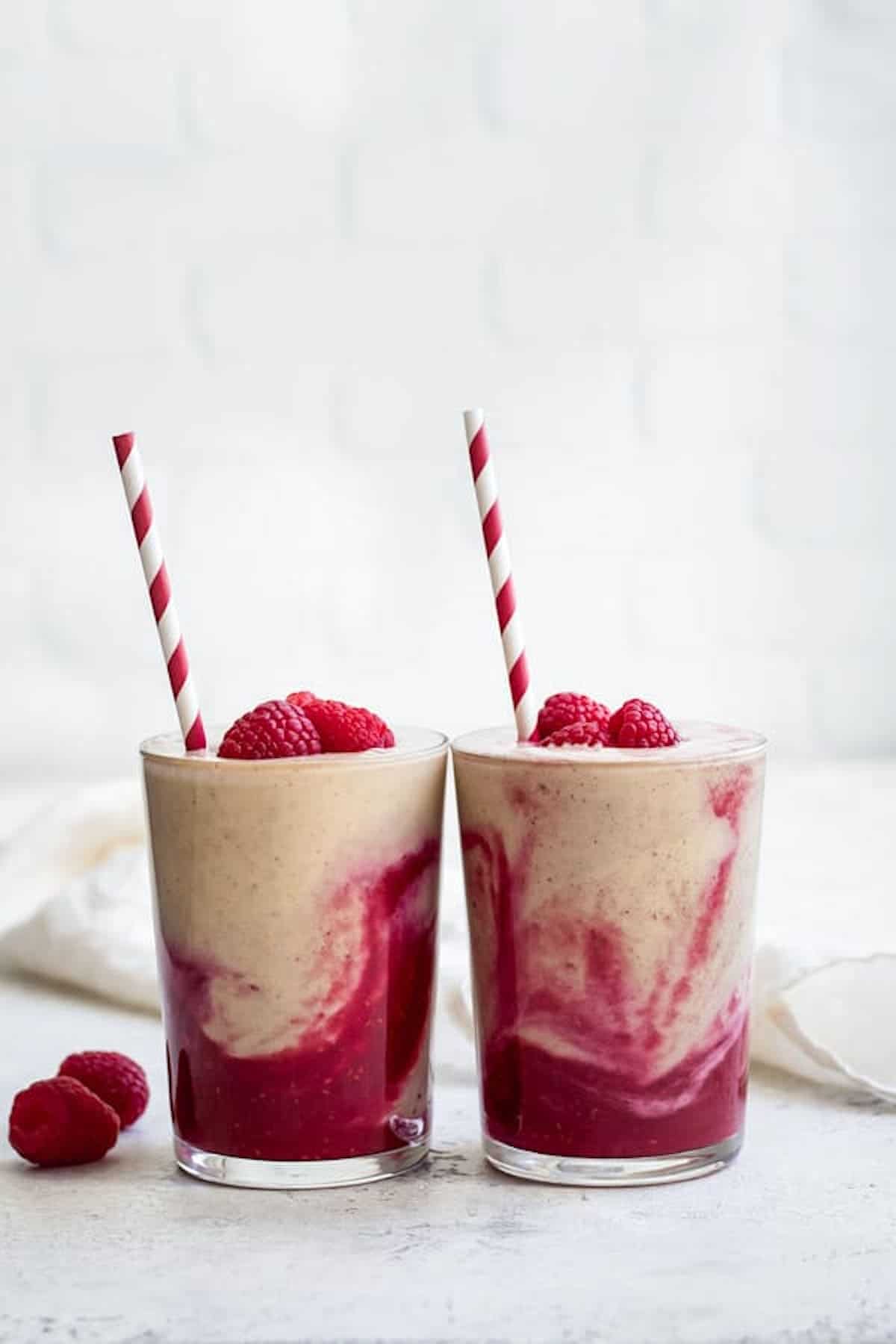 Two peanut butter and jelly smoothies side by side with raspberries on top