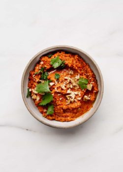 a ceramic white bowl with roasted red pepper dip topped with crushed walnuts and parsley