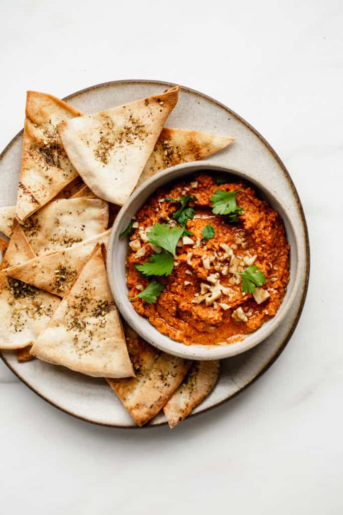 a bowl of roasted red pepper dip with pita chips on the side