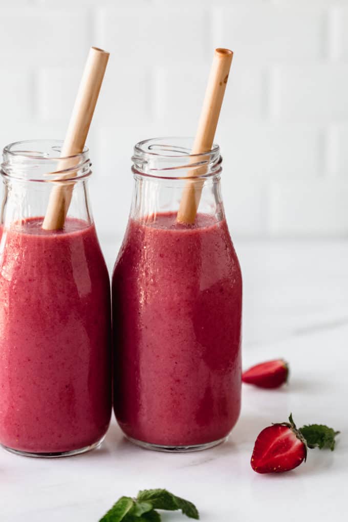 a red berry smoothie on a marble board with a bamboo straw