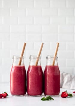 three bottles of berry smoothie with bamboo straws in them