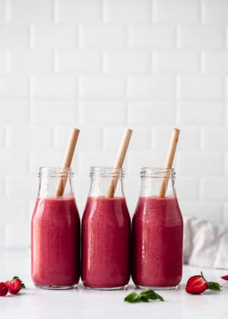 three bottles of berry smoothie with bamboo straws in them