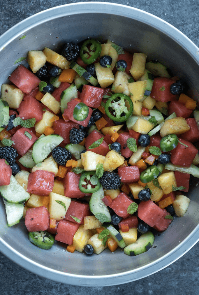 a silver mixing bowl filled with fruits to make summer salads, sliced jalapeno and fresh mint