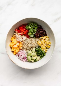 A large mixing bowl with quinoa, black beans, corn, avocado, jalapeno, red onions, mango, almonds, red pepper and cilantro in it
