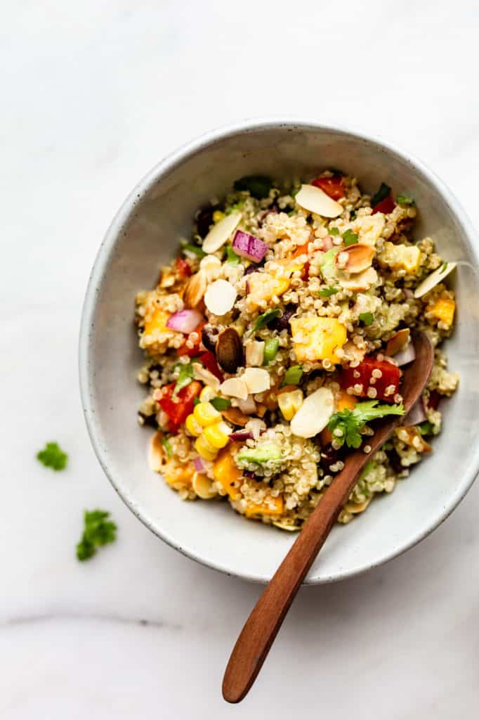 Southwest quinoa salad in a white bowl with a wooden spoon in it