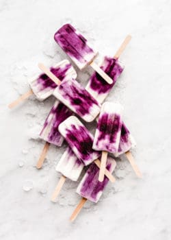blueberry greek yogurt popsicles stacked on ice on a marble board