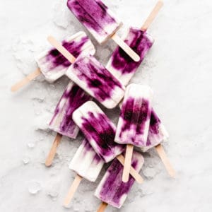 blueberry greek yogurt popsicles stacked on ice on a marble board