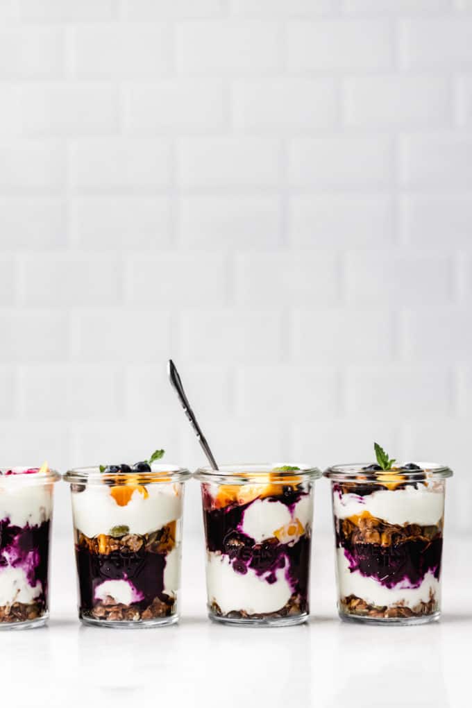 four jars of yogurt and granola parfaits with blueberry, mango and mint
