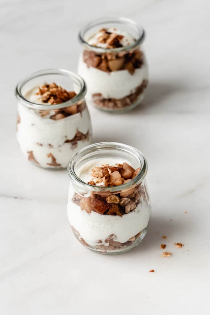 three jars of apple pie parfaits with layers of yogurt, granola and cooked apples
