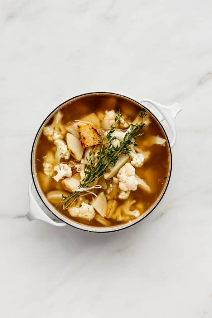 a white pot with roasted garlic, potatoes, cauliflower and thyme in it