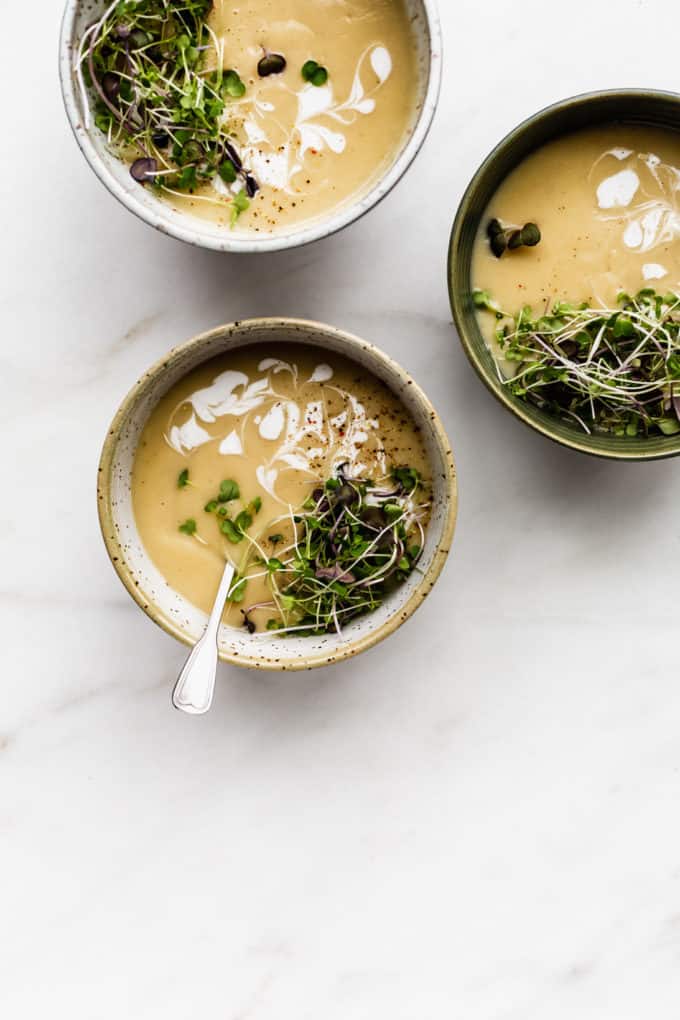 three bowls of roasted garlic soup with radish sprouts on top