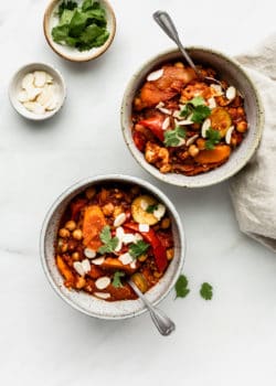 two bowls of vegetable tagine with two small bowls of almonds and cilantro on the side