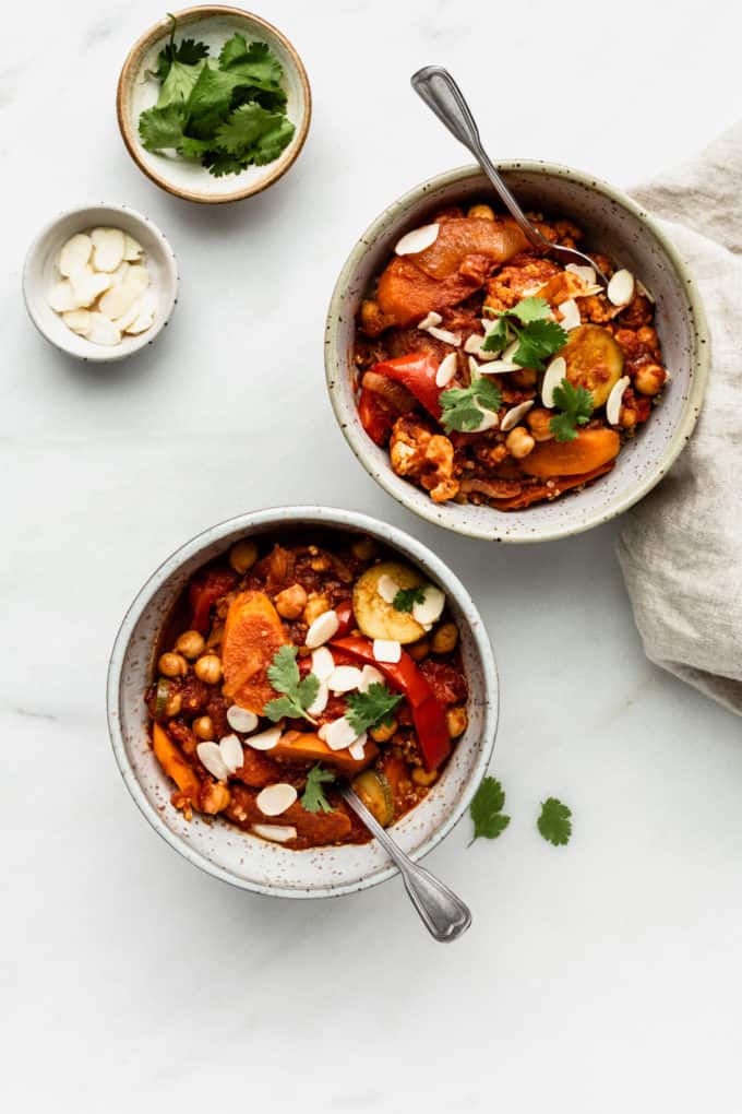 two bowls of vegetable tagine with two small bowls of almonds and cilantro on the side