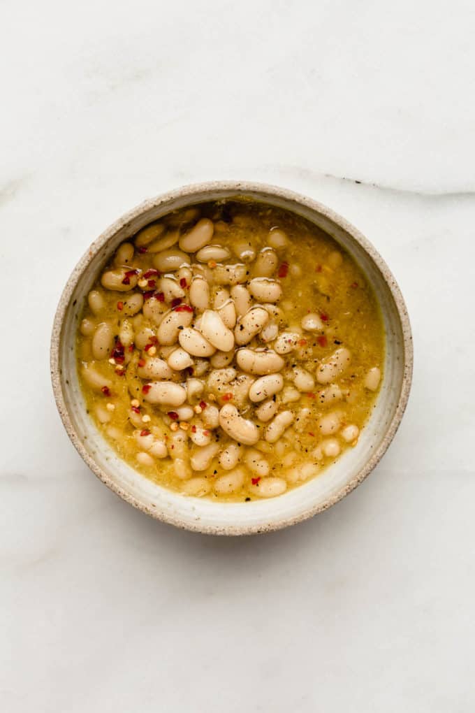 a bowl of white beans in broth topped with chili flakes