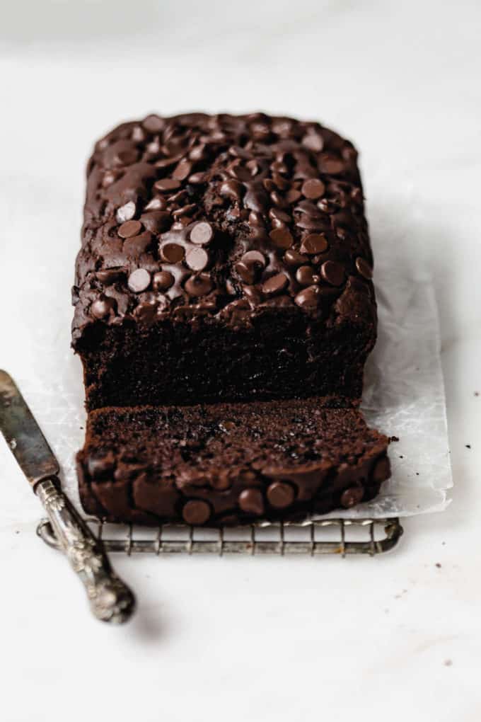 A loaf of healthy chocolate pumpkin bread topped with chocolate chips with a small knife on the side