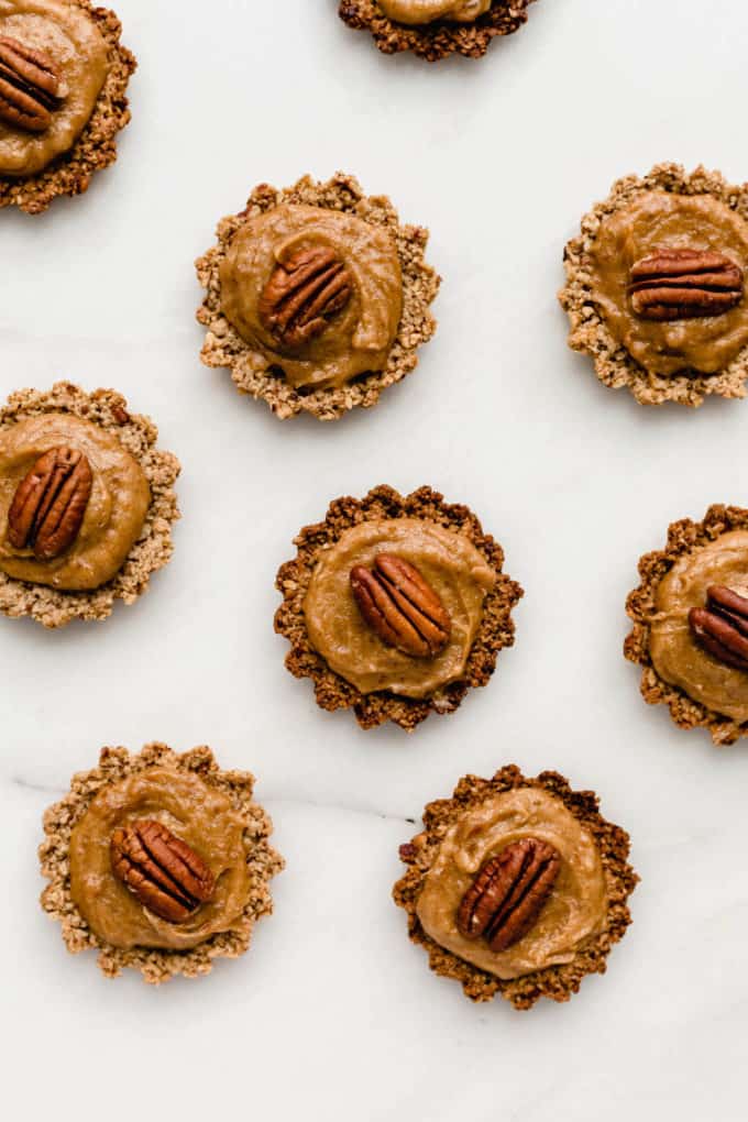 mini pecan pies topped with a pecan on a white marble board