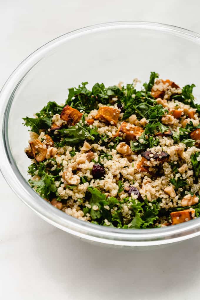 A clear mixing bowl of quinoa and kale salad with sweet potatoes