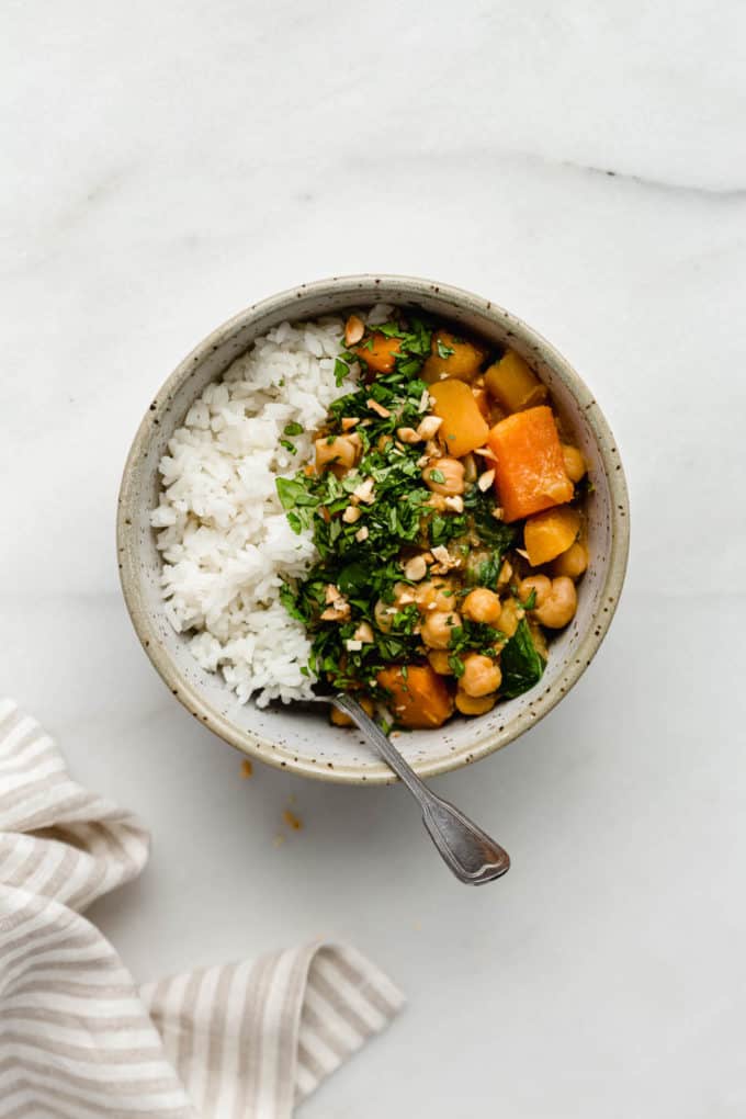 A bowl filled with white rice and pumpkin chickpea curry topped with cilantro and peanuts