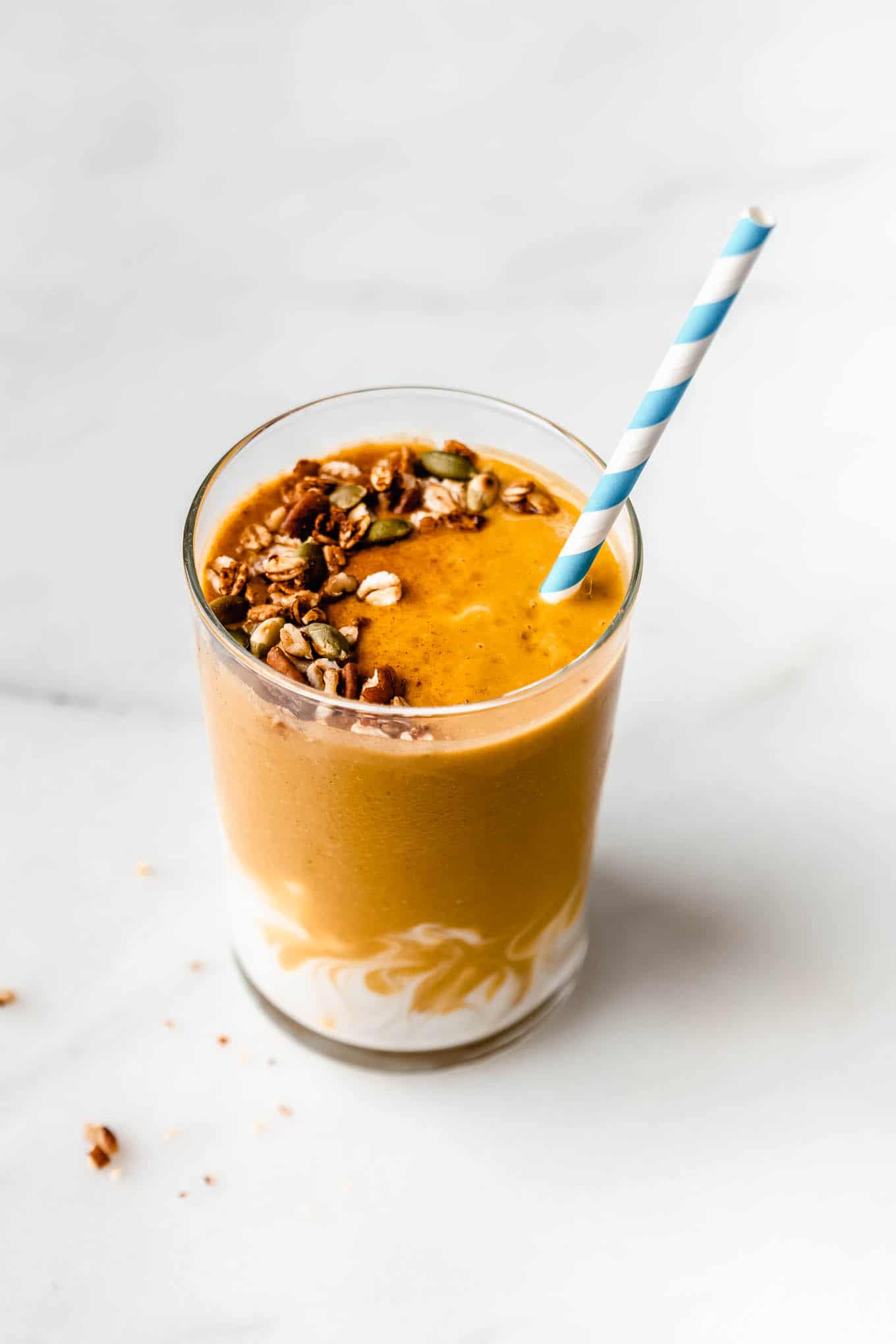 a pumpkin pie smoothie topped with granola with a striped blue and white straw in it