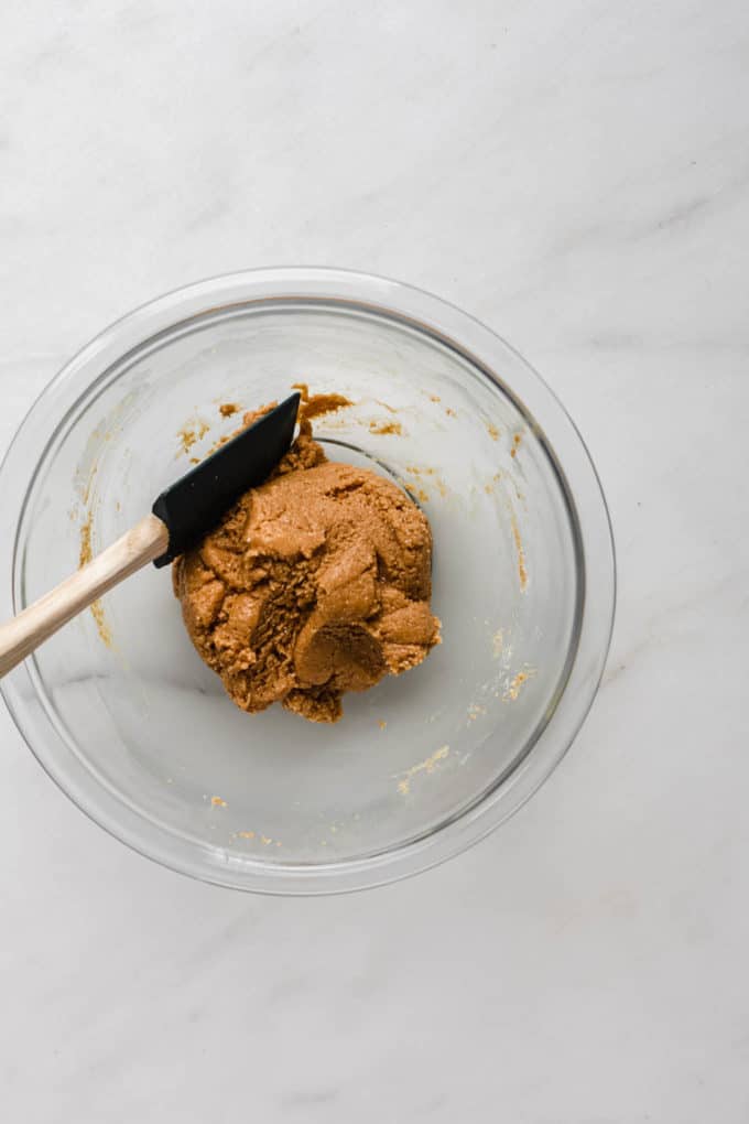 a clear mixing bowl with a wooden spatula and peanut butter dough in it