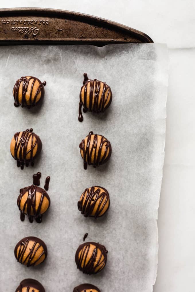Peanut butter buckeyes on a baking sheet with dark chocolate drizzled on top of them
