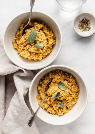 Two white bowls with risotto with butternut squash in them with a napkin on the side