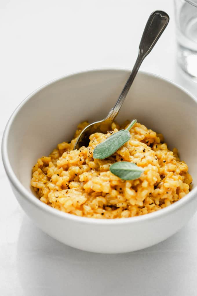 A white bowl wit orange risotto in it topped with sage leaves