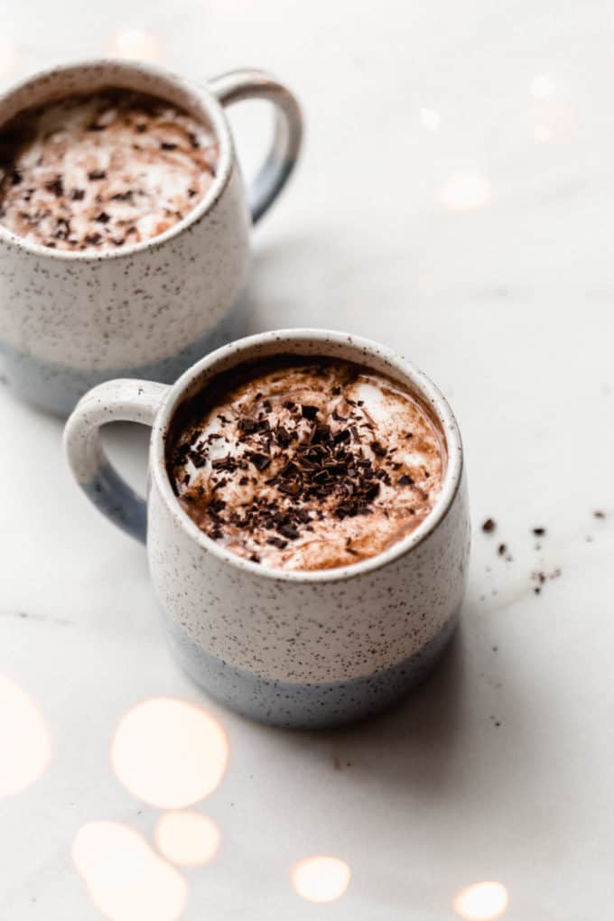 Two white speckled cups with vegan hot chocolate in them topped with chocolate shavings
