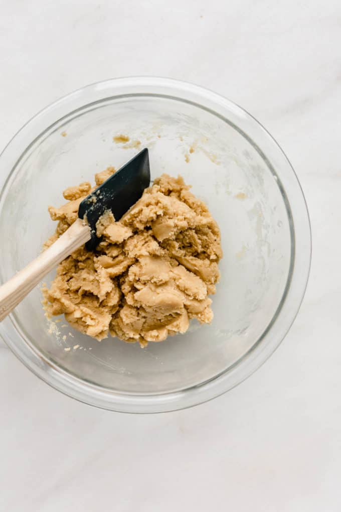 A clear mixing bowl with a spatula and cookie dough in it