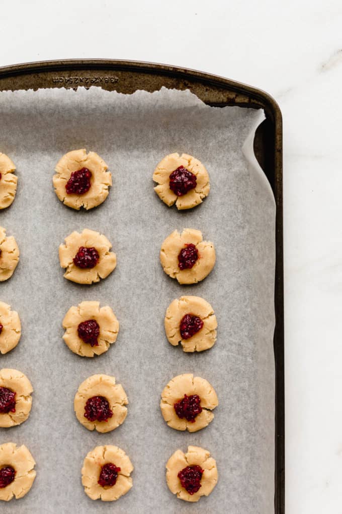unbaked thumbprint cookies with raspberry jam on a baking sheet