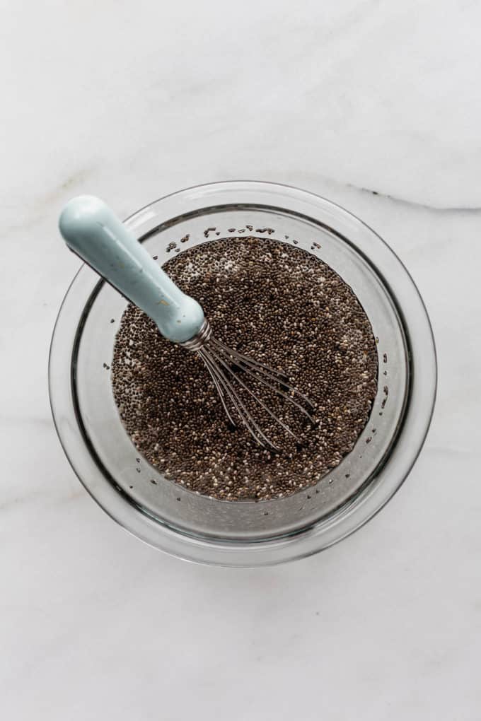 chia seeds and water in a clear mixing bowl with a whisk