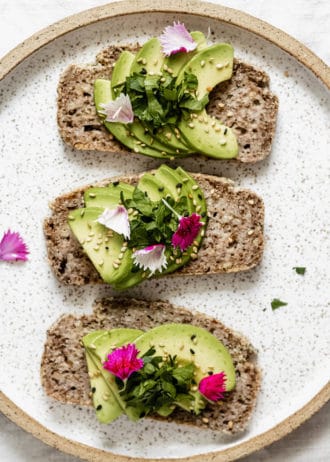 three slices of avocado toast on a plate topped with pink flower petals