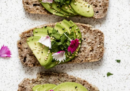 three slices of avocado toast on a plate topped with pink flower petals