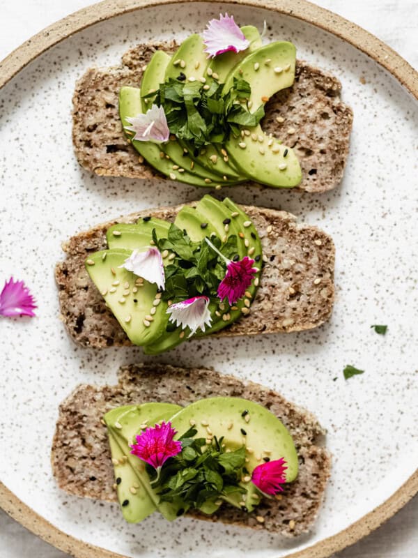 three slices of avocado toast on a plate topped with pink flower petals