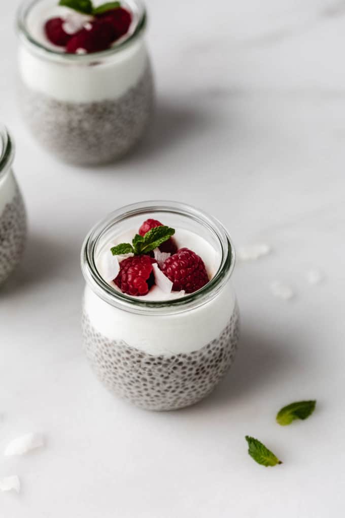 A jar of keto vanilla chia pudding topped with a layer of yogurt and three raspberries
