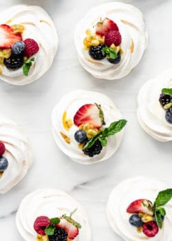 mini pavlovas on a white marble counter topped with fresh fruit and mint leaves