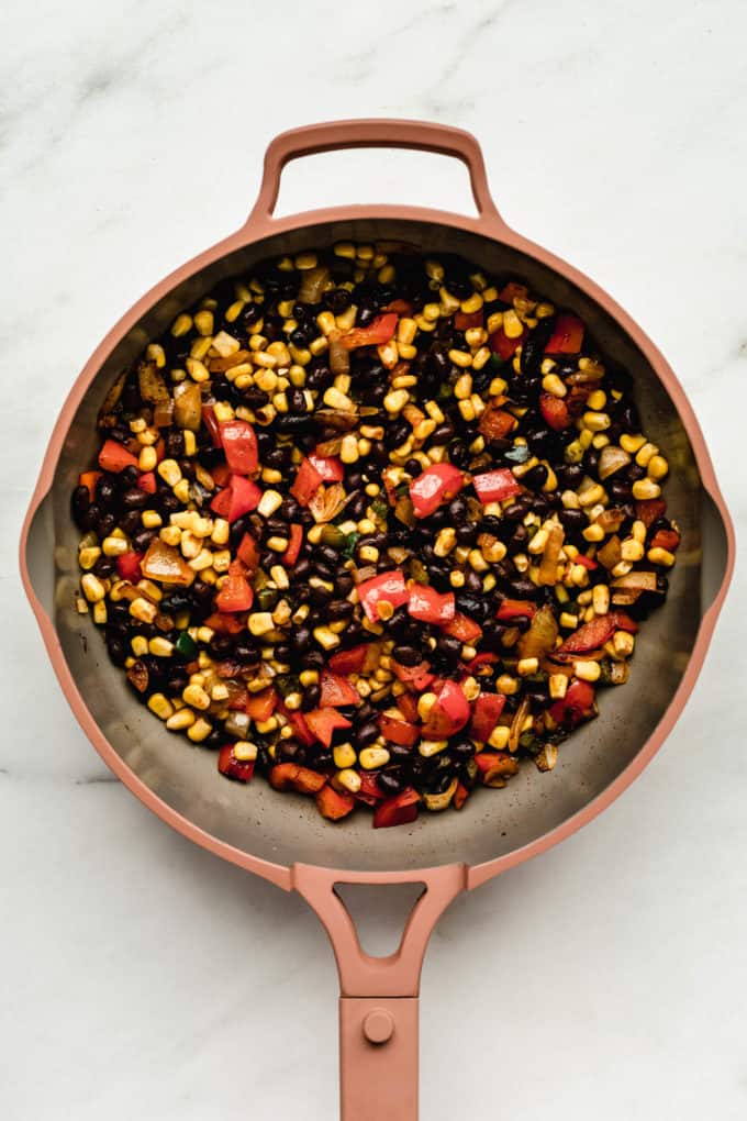 A pink pan with peppers, onions, corn and beans in it