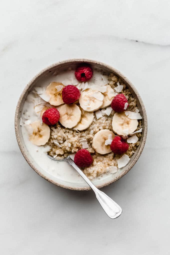Quinoa in a ceramic bowl with coconut milk bananas and berries in it