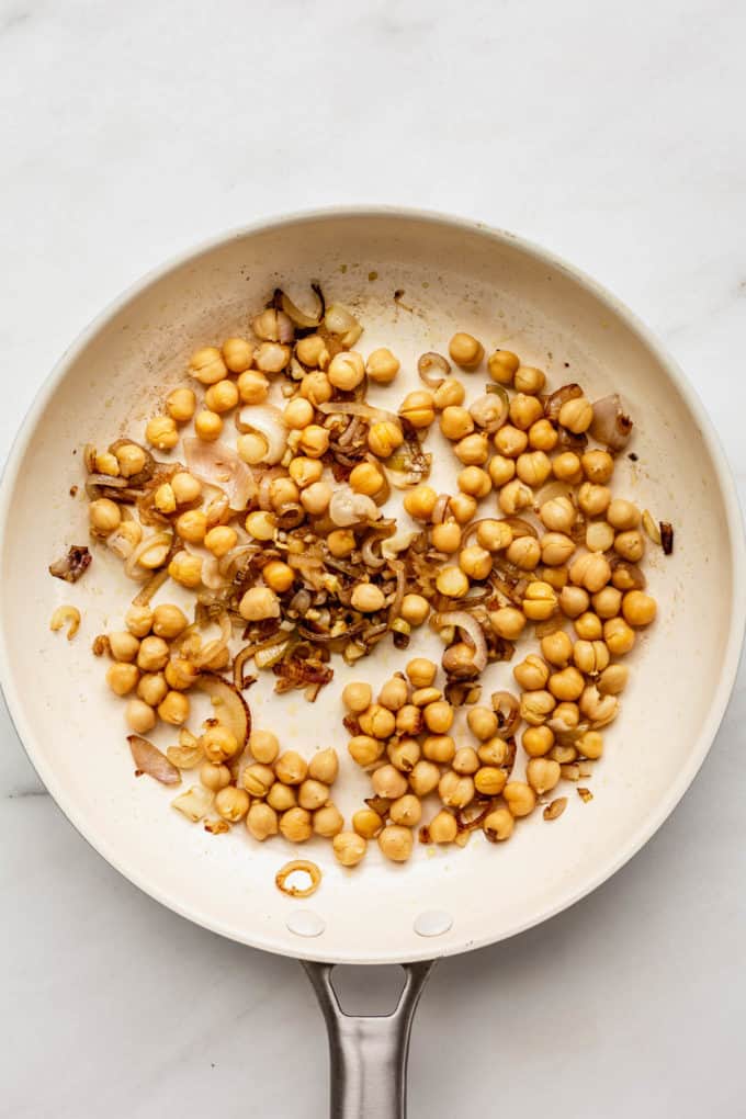 A white pan with chickpeas and shallots in it