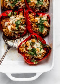 Quinoa stuffed red bell peppers topped with melted cheese in a white baking dish