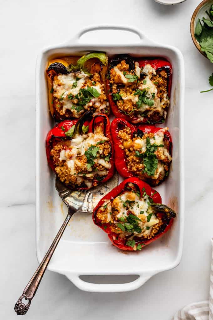 quinoa stuffed peppers in a white baking dish with a serving spoon