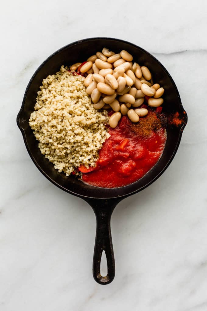 A cast iron skillet with red peppers, crushed tomatoes, white beans and quinoa