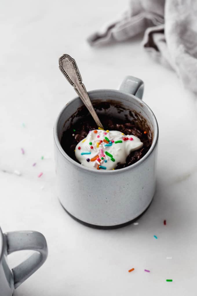 A chocolate mug cake in a grey mug topped with whipped cream and rainbow sprinkles