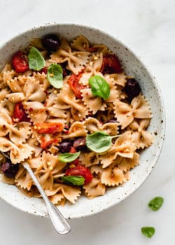 A bowl of farfalle pasta with olives, roasted tomatoes and basil