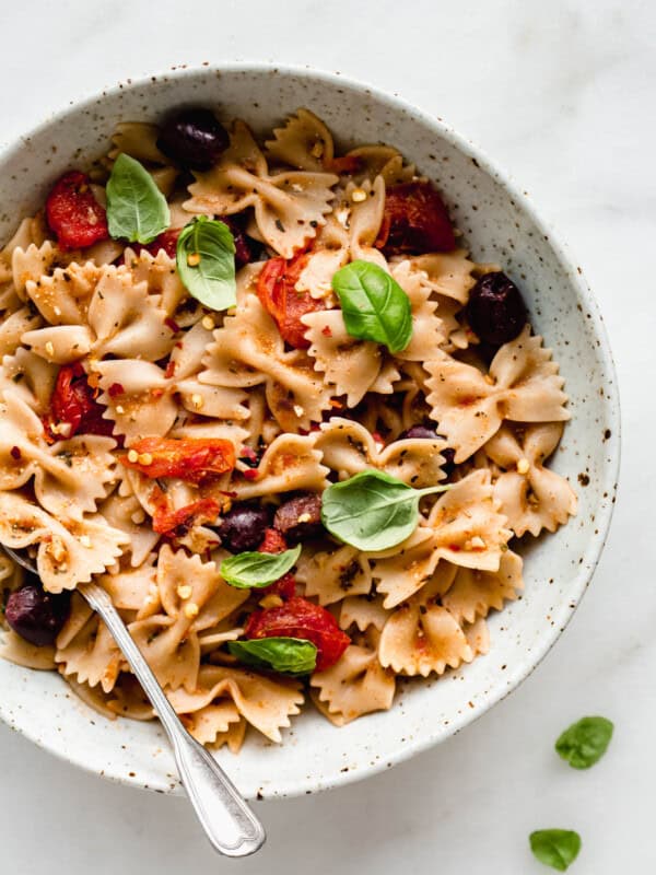 A bowl of farfalle pasta with olives, roasted tomatoes and basil