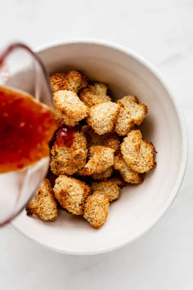sauce being poured into a bowl of panko crusted cauliflower