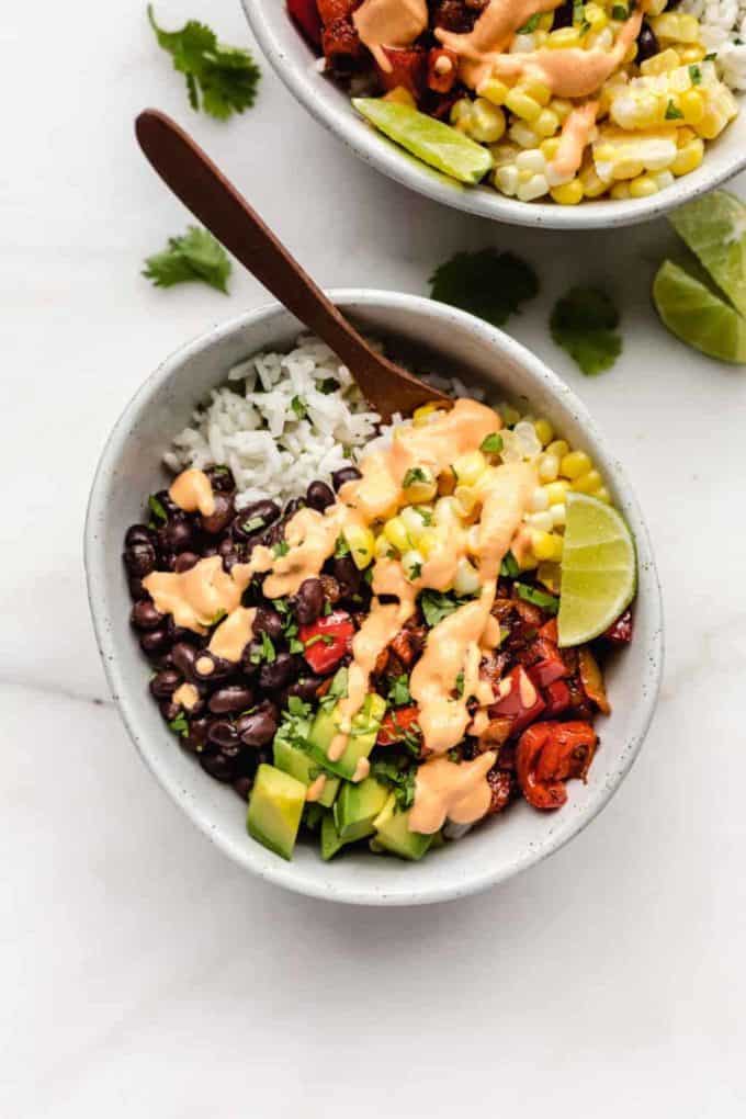 A burrito bowl with corn, beans, avocado and rice topped with chipotle cream